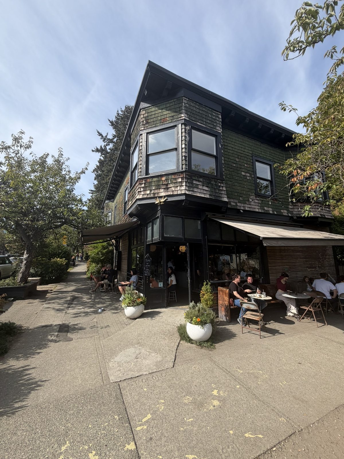 The corner of Le Marché St. George seen from the sidewalk, with its bay windows above the awning and people at tables below