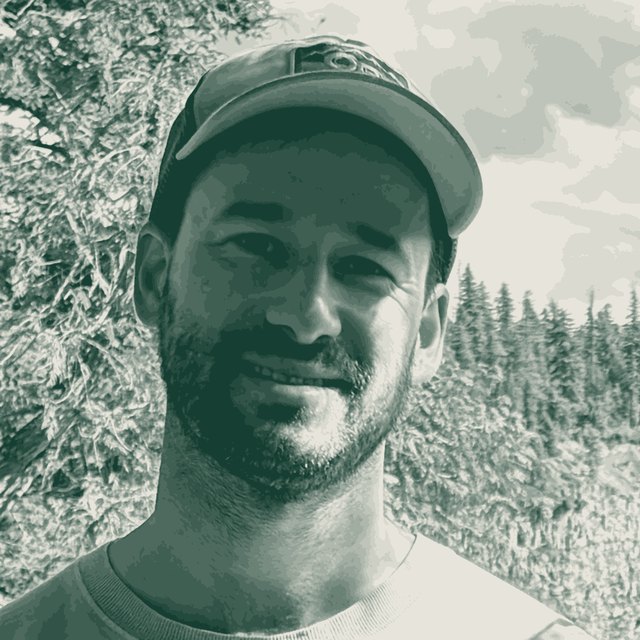 Konrad, who writes Side Street Vancouver, outdoors in a cap in front of trees and a waterfall